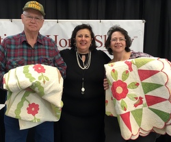 Dr. Lori standing with father and daughter holding quilts